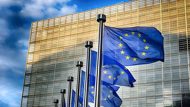 Row of EU flags against a gold glass facade under a cloudy blue sky